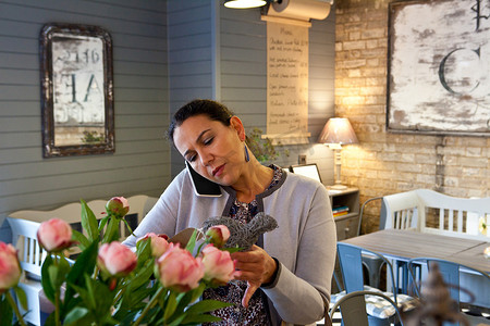 咖啡馆里成熟的女性顾客一边用智能手机聊天一边阅读菜单