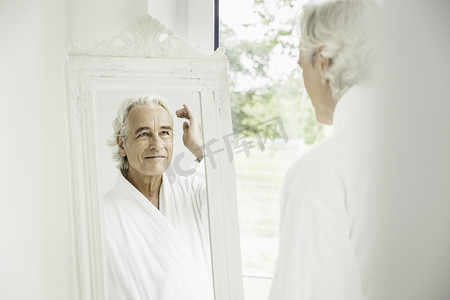 老人用牙线剔牙摄影照片_快乐的灰发老人穿着浴袍照镜子
