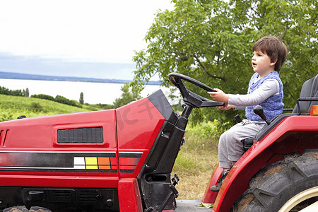 农机方向盘摄影照片_在花园里假装开拖拉机的男童