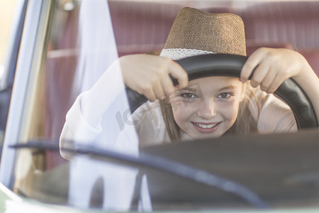 坐在汽车驾驶座上的年轻女孩握着方向盘微笑着