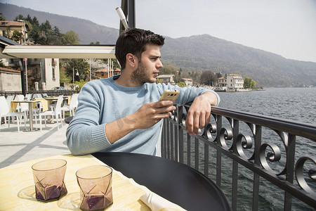 年轻男子从意大利皮埃蒙特韦尔巴尼亚梅尔戈佐湖湖边餐厅向外看