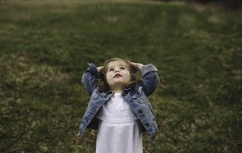 年轻的女孩在草地上双手放在头上仰望天空