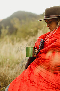 美国加利福尼亚州红杉国家公园一名妇女坐在乡村环境中裹着睡袋手持锡杯矿泉王