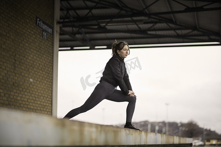机械转轮摄影照片_女跑步者在仓库平台上前倾伸展身体