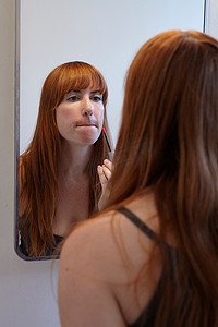 唇牙摄影照片_中年女性在镜子里涂唇彩