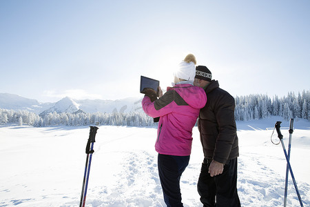 用数码平板电脑拍摄奥地利蒂罗尔山脉的高龄夫妇在雪地上的背影