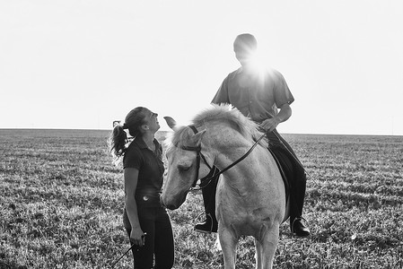 田野中骑着灰马的女子与男子聊天的黑白图像