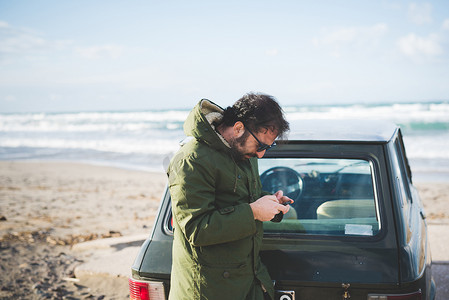 一名男子开着老爷车在海滩上阅读智能手机短信索尔索萨萨里意大利撒丁岛
