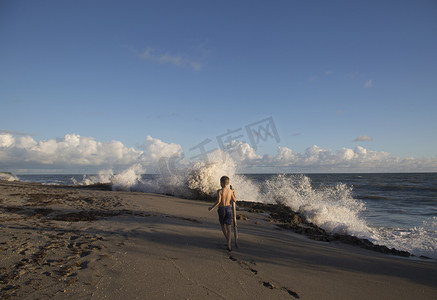 石凯摄影照片_美国佛罗里达州朱庇特岛男孩探索溅起海浪的海滩吹石保护区的后景
