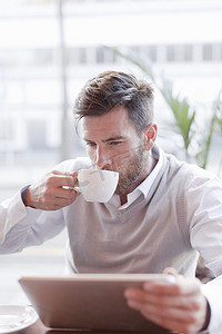 商务喝咖啡摄影照片_成熟的男人坐在咖啡馆里喝咖啡使用数字平板电脑