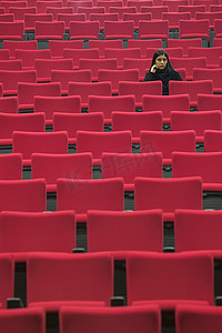一个女人独自坐在大厅里空的红色座位上