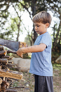 在花园里的柴堆上锯树枝的男孩