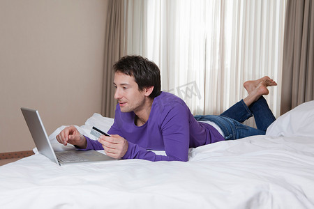 男人躺在酒店的床上带着笔记本电脑