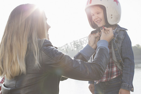 一名年轻女子给女儿戴上防撞头盔微笑着