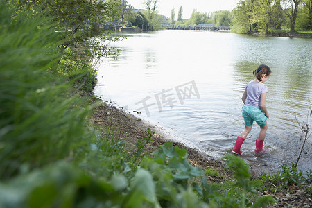 涉水摄影照片_穿雨鞋的女孩在池塘里涉水