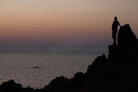 日落时在岩石上看海的人的剪影卡波特斯塔加卢拉撒丁岛意大利