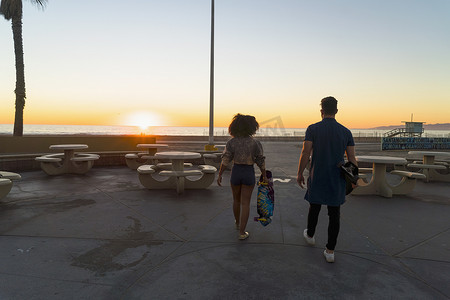 一对情侣在海滩附近散步手持滑板后视