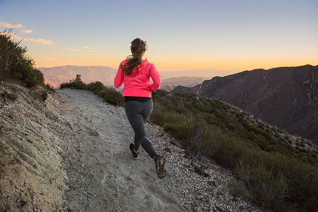 在公路上奔跑摄影照片_黄昏时分美国加利福尼亚州松树谷太平洋山脊步道上的年轻女子小径在土路上奔跑的背影