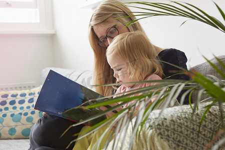 中年妇女和蹒跚学步的女儿在客厅沙发上阅读