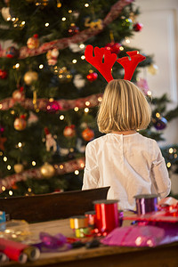 带鹿角的孩子摄影照片_圣诞树旁女孩的背影