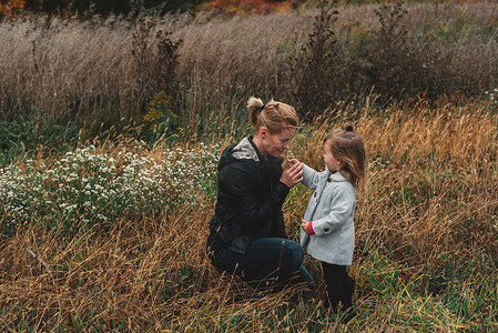 中年妇女和蹒跚学步的女儿在长草的田野里闻着野花的味道