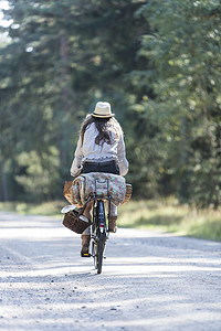 森林骑车摄影照片_背着觅食篮子在林间小路上骑车的妇女