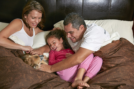 女孩躺在床上父母抚摸着小狗微笑的高视角