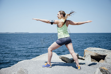 海边岩石上戴着活动跟踪器的女人的全身后视张开双臂锻炼