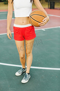 运动鞋摄影照片_一名年轻女子在球场上打篮球