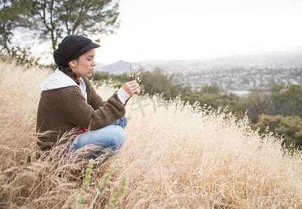 思考的小动物摄影照片_年轻女子蹲在长满青草的小山上手里拿着干草
