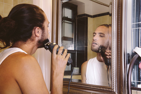 年轻人照镜子用电动剃须刀刮胡子