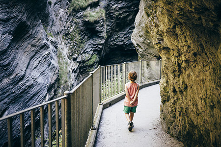 在蜿蜒穿过群山的高架人行道上男孩双手背朝后行走的背影瑞士