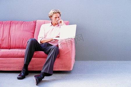 坐在沙发上的男子使用笔记本电脑