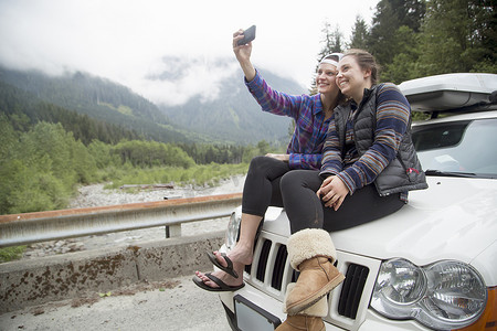 共享汽车摄影照片_徒步旅行者在汽车引擎盖上用智能手机自拍美国华盛顿州布兰科湖