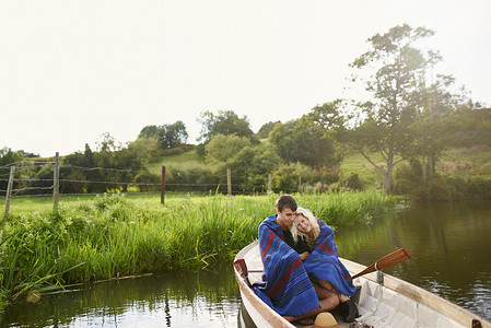年轻夫妇裹在河里划艇的毯子里