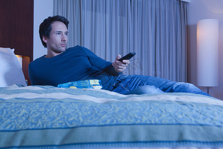 一名男子躺在酒店床上看电视