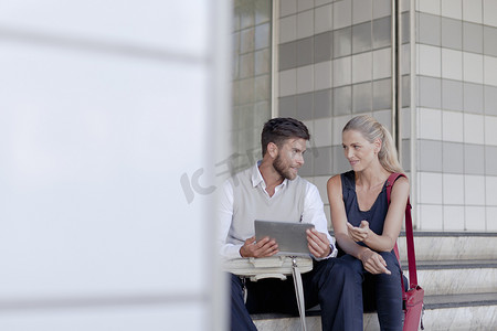 成熟的男人和女人坐在户外看着数字平板电脑