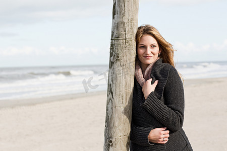 公司柱子摄影照片_一名女子靠在海滩上的柱子上
