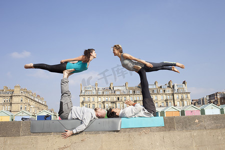对称摄影照片_布莱顿海滩上的男男女女在墙上练习杂技瑜伽