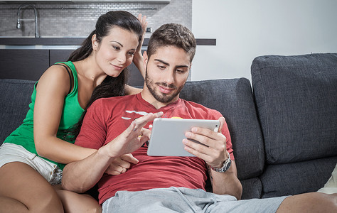 坐在沙发上使用数字平板电脑的年轻夫妇