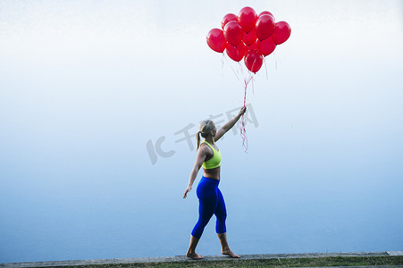 妇女手持一串红色气球的侧视
