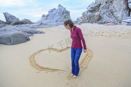 洗脚摄影照片_海滩上的中年妇女用脚画心形