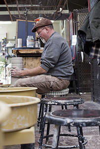 侧观作坊里的陶工坐在陶轮前塑造陶罐