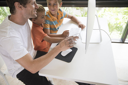 一名男子向两个儿子展示如何使用台式电脑