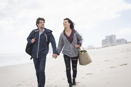 南非西开普省一对浪漫的年轻夫妇在狂风肆虐的海滩上漫步