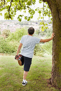 一条腿站立摄影照片_成熟男子在公园里伸腿