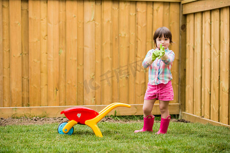 推着玩具手推车的年轻女孩戴上园艺手套