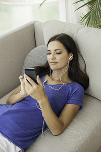 一位年轻女子斜靠在沙发上用智能手机听音乐