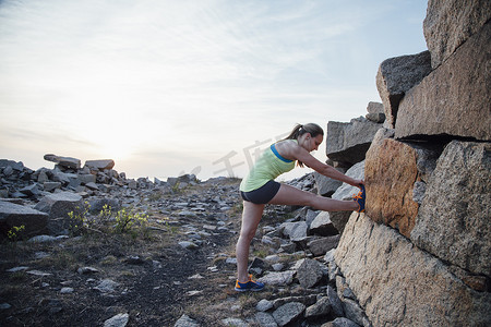 侧视女性抬起的腿靠在岩石上伸展