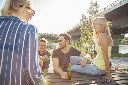 四个年轻的朋友在河边的野餐长凳上喝啤酒